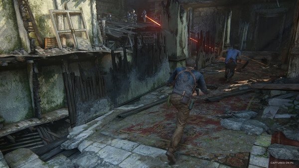 A screenshot from UNCHARTED: Legacy of Thieves Collection showing two characters fleeing through a damaged building under enemy fire.