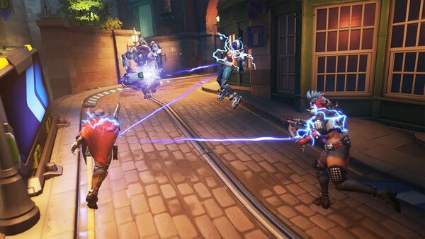 Overwatch® screenshot: Characters engage in a dynamic street battle, with energy beams connecting opponents in a vibrant urban setting.