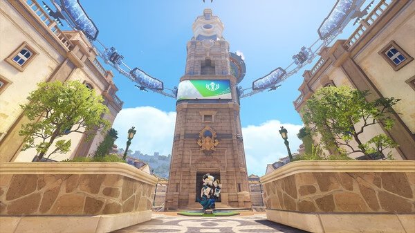 A screenshot from Overwatch® showing a character standing in front of a tall clock tower in a sunlit plaza.