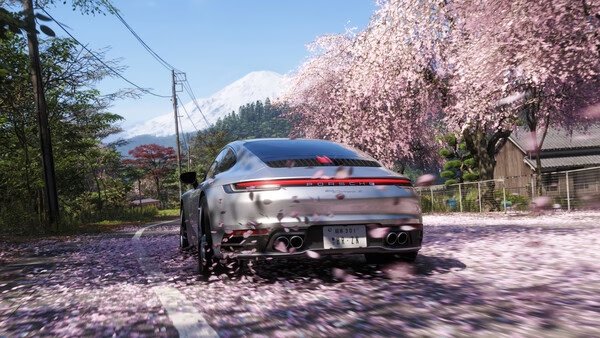 Forza Horizon 6 screenshot: A sleek car speeds through a scenic road lined with cherry blossoms, petals swirling in the air.