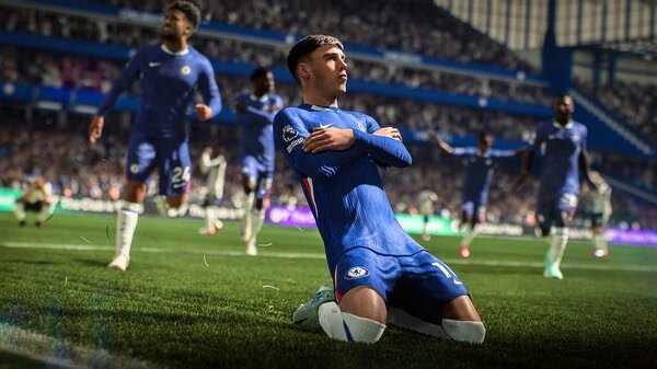 A screenshot from EA SPORTS FC™ 26 showing a soccer player in a blue jersey celebrating a goal by sliding on the grass.
