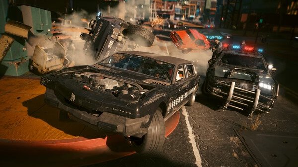 A Cyberpunk 2077 screenshot showing a chaotic car chase with vehicles crashing amidst smoke and debris on a city street.
