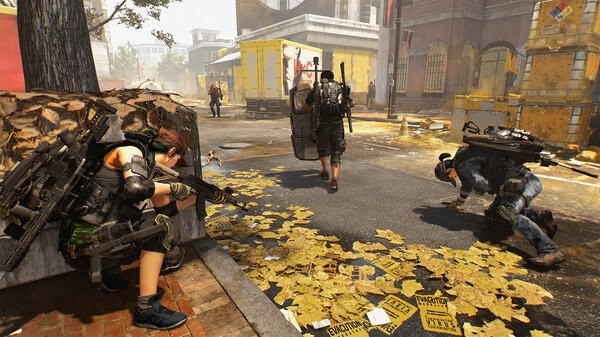 Screenshot from Tom Clancy’s The Division® 2 showing agents in combat gear taking cover and engaging enemies on a debris-filled urban street.