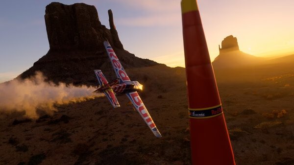 A screenshot from Microsoft Flight Simulator 2024 showing a Red Bull plane flying near a pylon at sunset in a desert landscape.