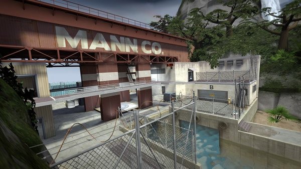 Team Fortress 2 screenshot showing the exterior of a Mann Co. facility, with a fenced area, water, and surrounding trees.