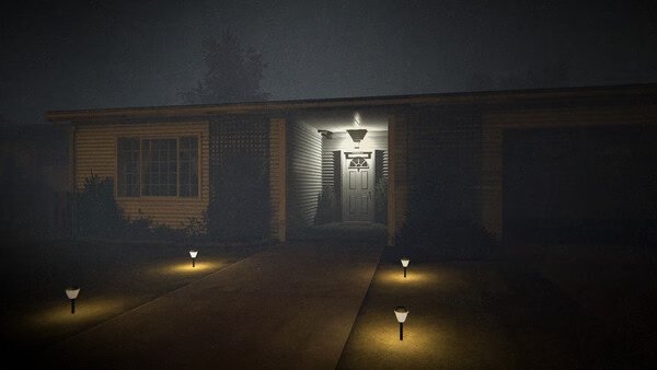 Phasmophobia screenshot: A dimly lit suburban house with a glowing porch light, surrounded by small pathway lights at night.
