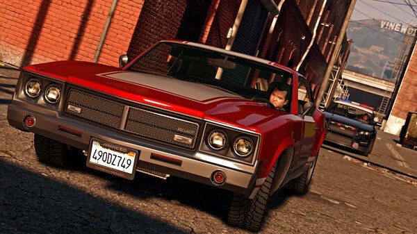 Grand Theft Auto V screenshot: A man drives a red and white car down a narrow urban street with another car following closely behind.