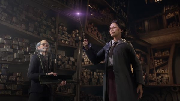 A screenshot from Hogwarts Legacy showing a character holding a glowing wand inside a shop filled with stacked wand boxes.