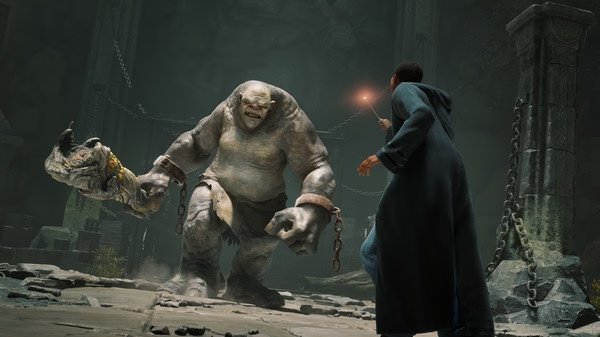Hogwarts Legacy screenshot: A wizard confronts a giant troll in a dimly lit stone chamber, wand raised for a spell.