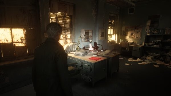 Silent Hill 2 screenshot: A man stands in a dimly lit, cluttered office with scattered papers and a glowing lamp on a desk.