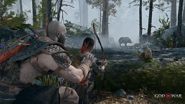 Kratos and Atreus crouch with bows drawn, aiming at a wild boar in the forest in this 'God of War' screenshot.