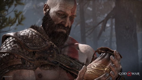 God of War screenshot: A close-up of Kratos holding a leather pouch, wearing armor, with a forest in the background.
