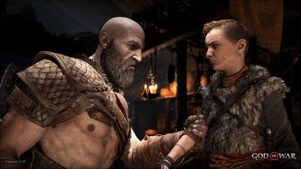 Screenshot from God of War showing a muscular, armored character shaking hands with a young person in a fur-lined outfit inside a dimly lit room.