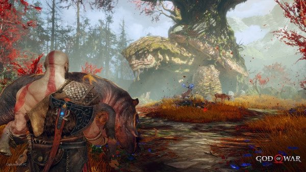 Screenshot from God of War showing Kratos carrying a boar in a vibrant forest with a large snake in the background.